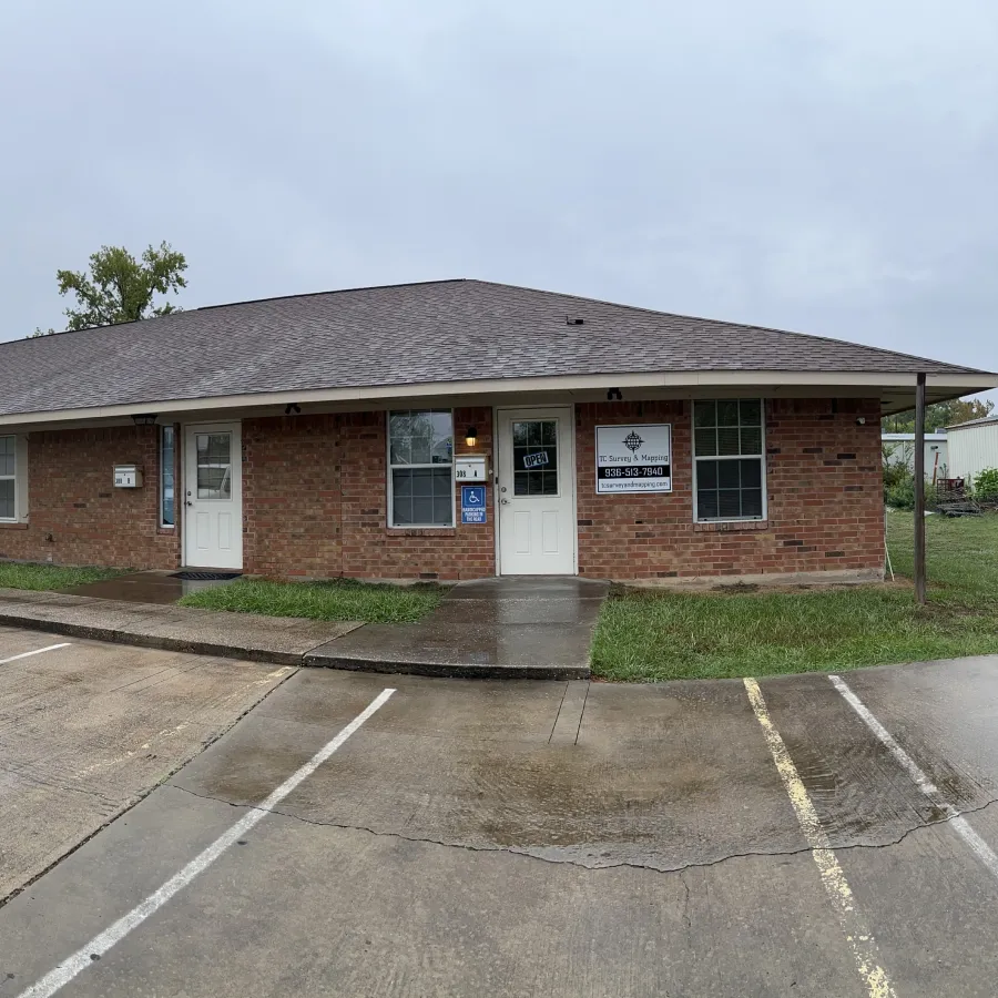 A white pickup truck parked in front of a brick building with a sign that reads, "TC Survey & Mapping".
